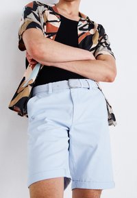 Chemise à motifs abstraits à manches courtes dans des teintes marron, bleu et crème, associée à un short en denim bleu clair retroussé et une ceinture tissée.