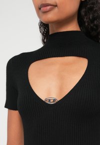 Top negru din tricot cu dungi, cu guler înalt și detaliu decupat cu un accent de logo metalic argintiu la bust. Mâneci scurte.