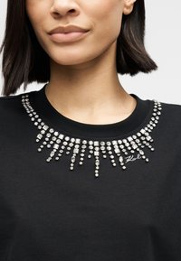 Μαύρο T-shirt με διακοσμητικό, λαμπερό ντεκολτέ από στρας με διαφορετικά μήκη. Υπάρχει διακριτική κέντημα με τη λέξη «Karl» κοντά στον γιακά.