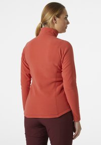 Fleece pullover in koraal met een hoge kraag. Heeft lange mouwen, vlakke naden en een getailleerde vorm voor comfort en bewegingsvrijheid.