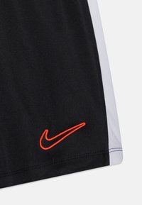 Svarta sportshorts med en framträdande orange Nike-logotyp, vita sidopaneler och tillverkade av lätt, texturerad tyg.