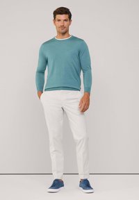 Light teal long-sleeve sweater with a white neckline, paired with white slim-fit pants and blue suede sneakers. Simple design and clean lines.