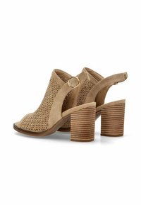 Zapatos de tacón abiertos en color beige con un diseño de cortes, que cuentan con un talón tipo slingback con una hebilla circular y un tacón grueso acanalado.
