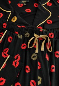 Must mustrill komplekt, millel on punane ja kuldne huuletõrjevormistus, kuldne ääristamine ning kuldse paelaga pingutav vöökoht. Pehme ja sile kangas.