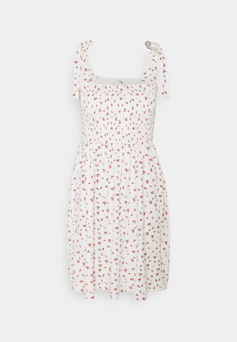 Robe blanche sans manches avec petit imprimé floral rouge et bretelles nouées aux épaules, dotée d'un corsage smocké et d'une jupe évasée.