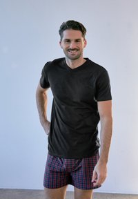 Schwarzes kurzärmliges T-Shirt mit V-Ausschnitt, kombiniert mit rot-blauen karierten Shorts. Glatter Stoff, figurbetontes Design und lässiger Stil.
