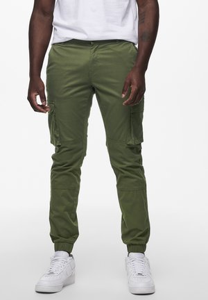 Groene cargo-broek met elastische boorden, voorzien van meerdere zijzakken en een gladde katoenen stof. Gepaarde met witte sneakers.