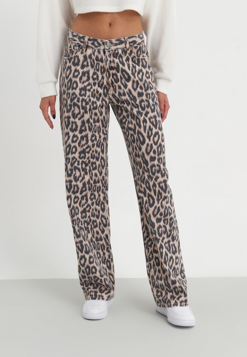 Jeans de estampado de leopardo em tom claro com manchas mais escuras. Design de pernas retas, cintura de altura média e costura em contraste. Usados com ténis brancos.