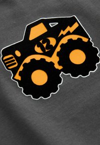 Schwarze und orange Grafik eines Monstertrucks mit großen Reifen auf einem grauen Stoffhintergrund, mit einem flachen Design und weicher Textur.