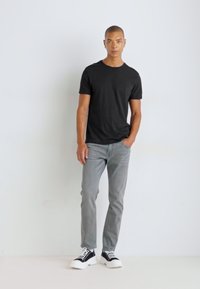 Camiseta negra de manga corta combinada con jeans gris claro y zapatillas blancas y negras; el conjunto tiene un diseño casual y ajustado.