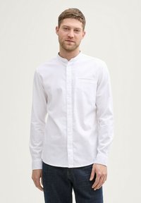 Camicia bianca con colletto alla coreana, dotata di una tasca sul petto e maniche lunghe, realizzata in morbido tessuto di cotone.