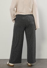 Spodnie z szerokimi nogawkami w teksturowanym ciemnoszarym materiale, z elastyczną talią. W połączeniu z jasnobeżowym, puszystym swetrem i kremowymi butami typu slip-on.