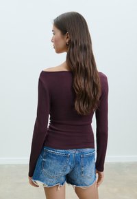 Bordeaux langemouwen top met een off-shoulder halslijn, gecombineerd met distressed denim shorts, die een casual, getailleerd ontwerp laat zien.