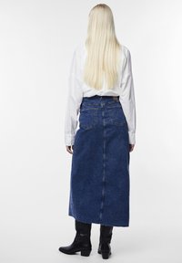 Sötétkék denim maxi szoknya, amely szoros derékrésszel, két hátsó zsebbel és egyenes fazonnal rendelkezik; fehér inggel és fekete csizmával párosítva.