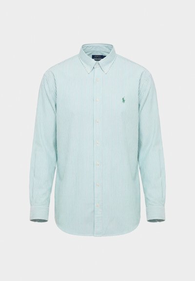 Košulja dugih rukava na kopčanje s gumbima, s uspravnim prugama u svijetloplavoj i bijeloj boji te malim vezenim logotipom na lijevoj strani prsa.