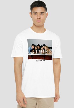 Young man wearing white T-shirt with a Friends TV show graphic of six people leaning on a counter with milkshakes.