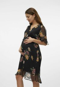 Zwarte zwangerschapsjurk met een V-hals, korte fladdermouwen en een gerimpelde zoom. Voorzien van kleurrijke bloemen in geel, roze en groen.