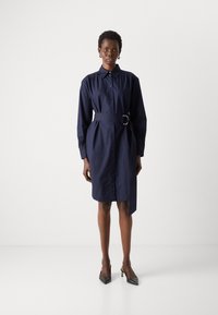 Navy-blauwe shirtjurk van katoen, met een knoopsluiting aan de voorkant, een ceintuur met een ronde gesp en lange mouwen. Gladde textuur.