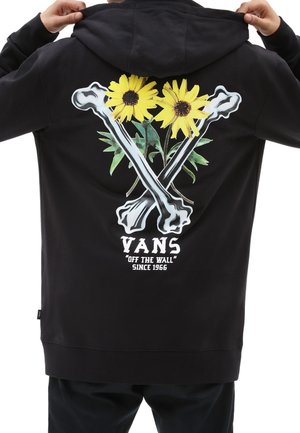 Svart hoodie med en grafisk design av två korsade ben med gula solrosor och gröna blad. Inkluderar "VANS"-logotyp och text.