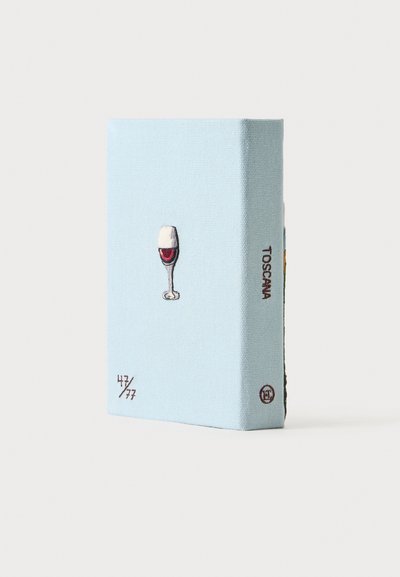 Livre bleu clair avec une petite illustration d'un verre à vin sur la couverture et le texte "TOSCANA" sur la tranche, debout sur une surface blanche.