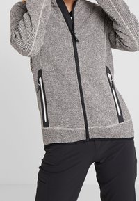 Chaqueta con cremallera a rayas grises y negras, con bolsillos laterales y detalles en negro. La tela parece texturizada y suave, con una silueta ajustada.