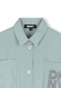 Chemise color menthe à col, avec un bouton à l'avant, deux poches poitrine et le logo DKNY brodé en gris sur la poche droite.