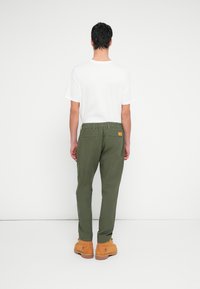 Zielone bawełniane spodnie dresowe z elastycznym pasem, dwoma tylnymi kieszeniami i zwężanymi nogawkami. Zestawione z prostą białą koszulką i brązowymi butami.