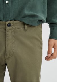 Khaki spodnie z teksturowanej, tkanej tkaniny; posiadają zapięcie na guzik, szlufki na pasek i boczne kieszenie. Połączone z ciemnozieloną koszulą.