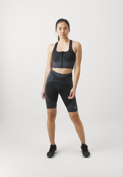 Black athletic crop top with a front zipper, paired with black compression shorts featuring contrasting textures and seams. Black sneakers.