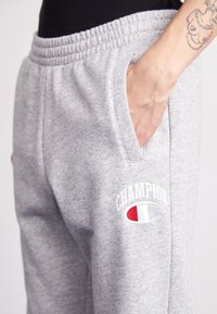 Gray sweatpants made of soft fabric with an elastic waistband, featuring side pockets and Champion logo in white, red, and blue embroidery.