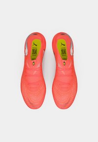 Par af klare orange Puma sportssko med sort Puma-logo indeni og QR-kode på gule indlægssåler, set oppefra på hvid baggrund.