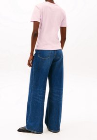 Světle růžové bavlněné tričko v kombinaci s volnými modrými denimovými džíny. Džíny mají klasický design s pěti kapsami a prošíváním na lemu.
