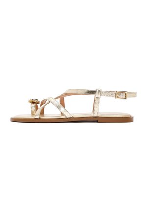 Sandalia plana dorada con finas tiras cruzadas, hebilla ajustable en el tobillo y adorno dorado decorativo cerca del lazo del dedo.