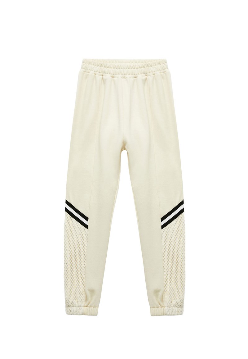 Cremefarvede sweatpants med mesh-paneler i siden, sorte striber på siderne og elastisk talje. Blød tekstur og tapered pasform.