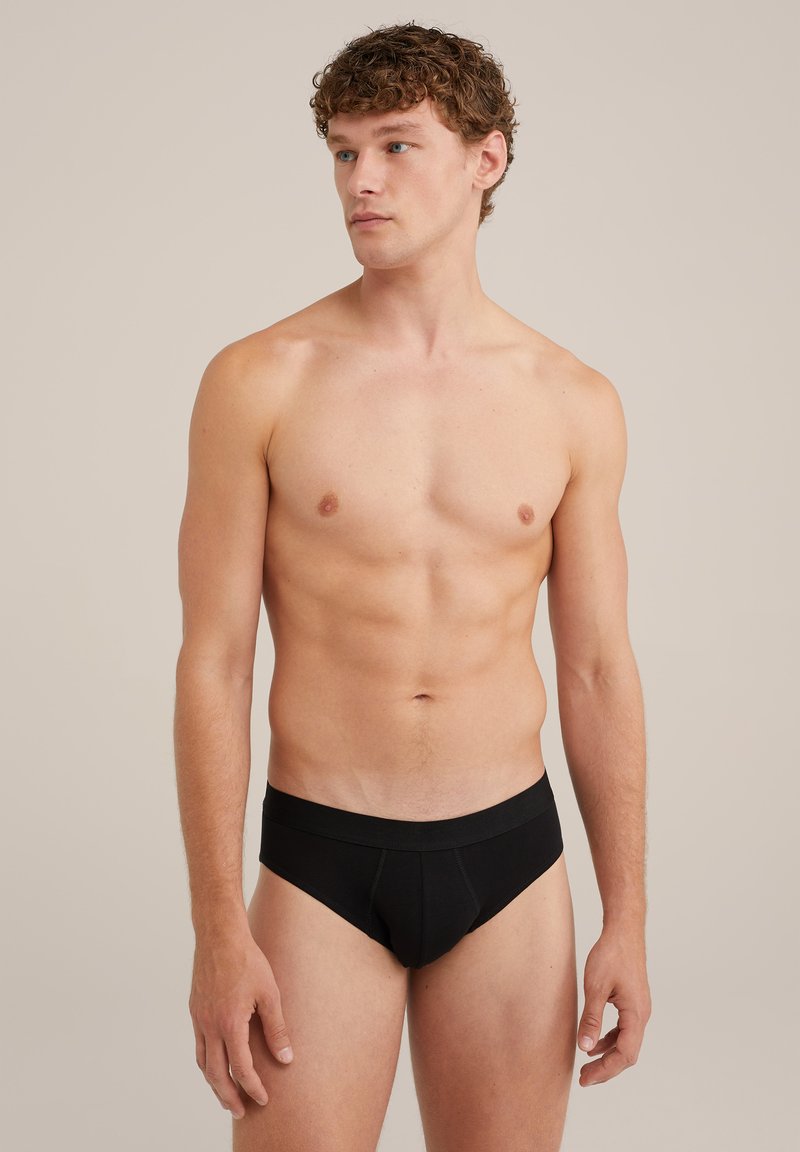 Svarta bomullshorts med bred midjeband, med en slät yta och formar en konturerad framficka. Modellen står i en neutral miljö.