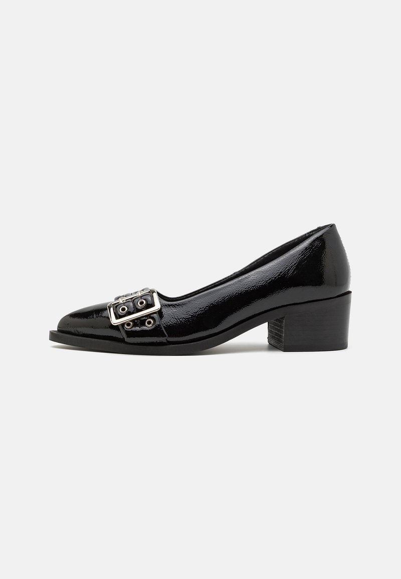 Escarpin en cuir verni noir avec bout arrondi, petit talon carré et double boucle sur le devant. Texture lisse et brillante.