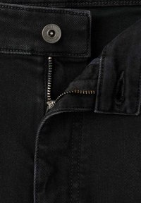 Jeans de mezclilla negra con botón de presión metálico, cierre de cremallera y tejido texturizado. Presentan costuras cosidas y una cintura lisa.