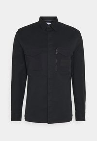 Camicia nera con bottoni, dotata di due tasche sul petto, una tasca con zip e un dettaglio a toppa. Realizzata in un tessuto resistente con una superficie liscia.