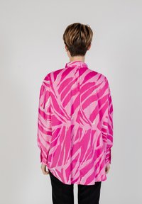 Blusa de manga larga en rosa brillante con un patrón abstracto de hojas blancas, con cuello tipo camisa y un corte suelto y relajado.