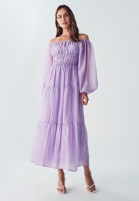 Vartalon paljastava laventelinvärinen maksimekko, jossa on kerrokselliset helmat, joustava vyötärö ja läpinäkyvät pitkät hihat, valmistettu kevyestä, teksturoidusta kankaasta.