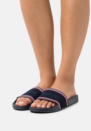 Sandales en slide navy avec un dessus en tissu texturé, rehaussées de détails blancs et rouges, présentant un design à bout ouvert et une semelle plate en caoutchouc noir.