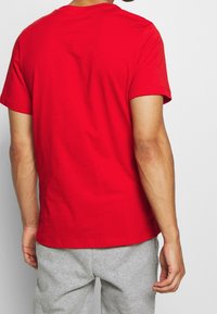Camiseta de algodón roja con mangas cortas, cuello redondo y textura lisa. Combinada con pantalones de chándal grises, que muestran un ajuste relajado.