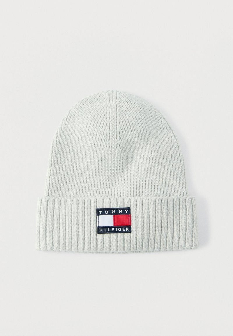 Bonnet gris clair en tricot avec un revers côtelé. Présente un patch logo rectangulaire en bleu marine, rouge et blanc.