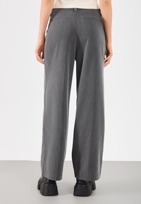 Sive široke hlače iz teksturirane tkanine, z višjim pasom in dvema zadnjima žepoma, stilizirane z masivnimi črnimi čevlji.