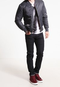 Svart bomberjacka, vit t-shirt med grafik, svarta jeans och vinröda högstövlar. Slät tyg, åtsittande design, avslappnad stil.