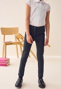 Pantaloni neri su misura con una vestibilità slim, dotati di tasche laterali e chiusura con bottone, abbinati a una camicia bianca con colletto a maniche corte.