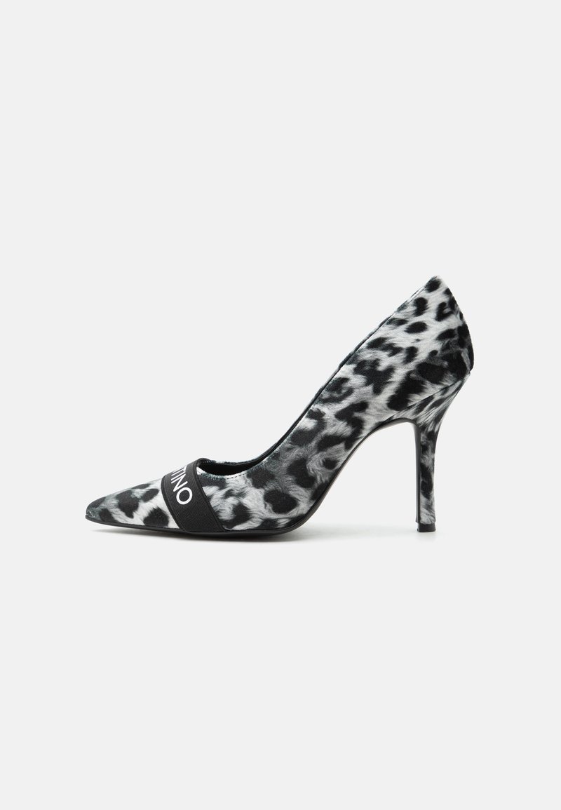 Escarpin à talon haut imprimé léopard noir et blanc avec bout pointu et une bride noire sur le devant sur un fond clair uni.