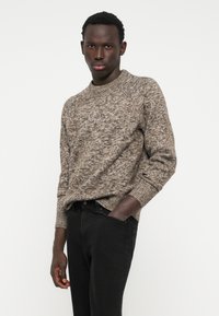 Knit sweater in a blend of brown tones with a textured pattern, crew neckline, and ribbed cuffs, paired with black jeans.