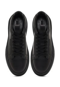 Le sneaker nere in pelle presentano una texture liscia, punta rotonda, design con lacci e accenti lucidi a contrasto sui lati.