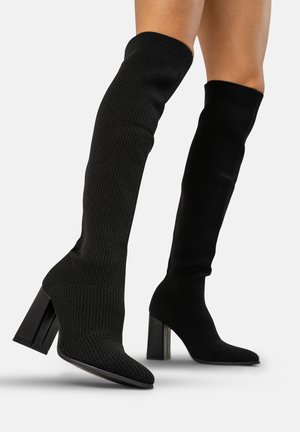 Knielange schwarze Stiefel aus strukturiertem Material mit spitzer Zehe und massiven Blockabsätzen. Verfügt über einen enganliegenden Schaft und gerippte obere Kanten.